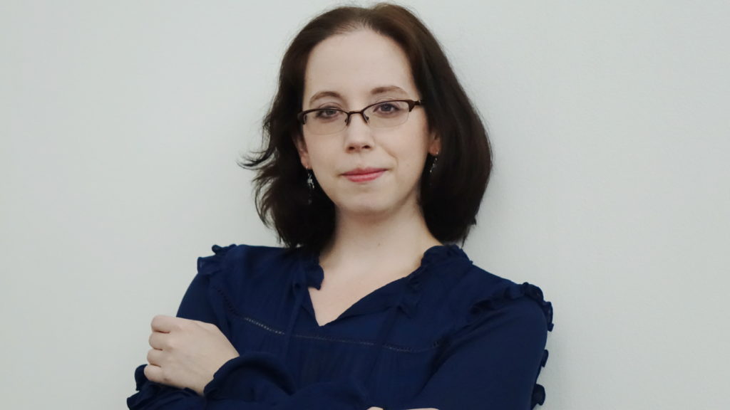 Alex in glasses and a navy colored shirt with her arms crossed, looking serious, competent, and approachable.